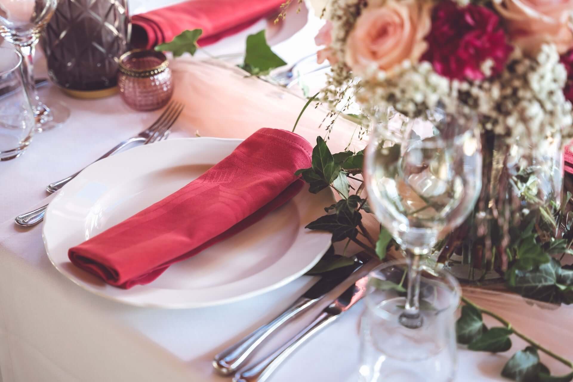 Formal table setting with white charger plate and red dinner napkin